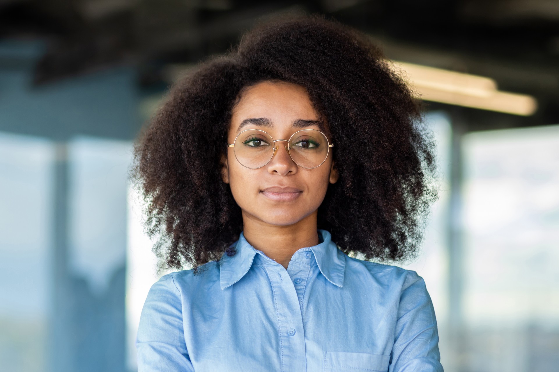 Serious concentrated woman close up, business woman looking thinking at camera, female worker with curly hair inside office at workplace