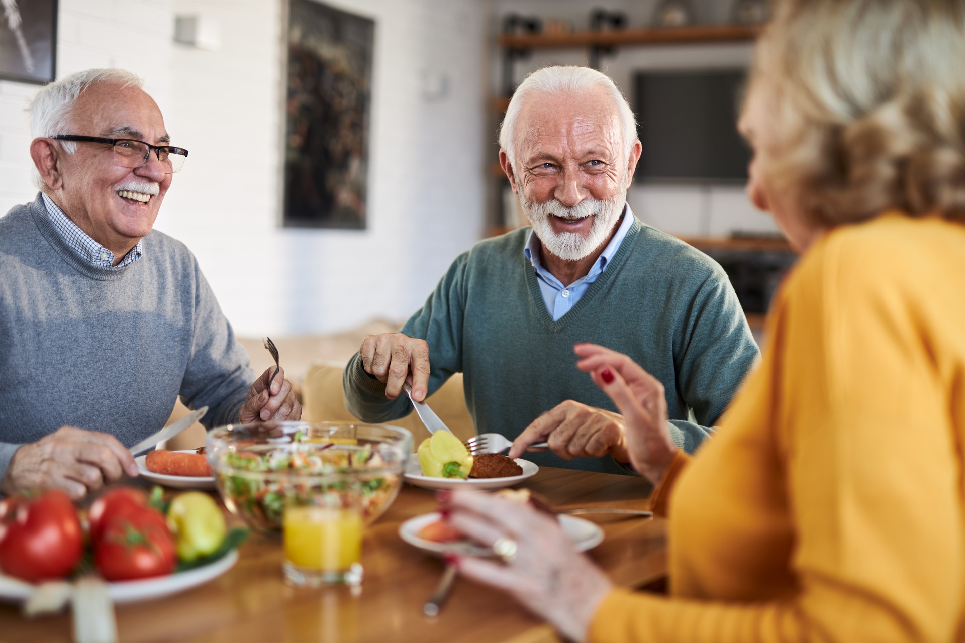 Group of happy senior friends talking while having a meal at dining table.